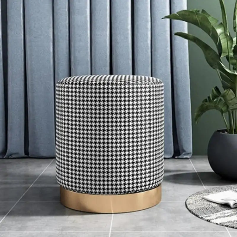 Patterned ottoman with gold base in a room setting with curtains and plant