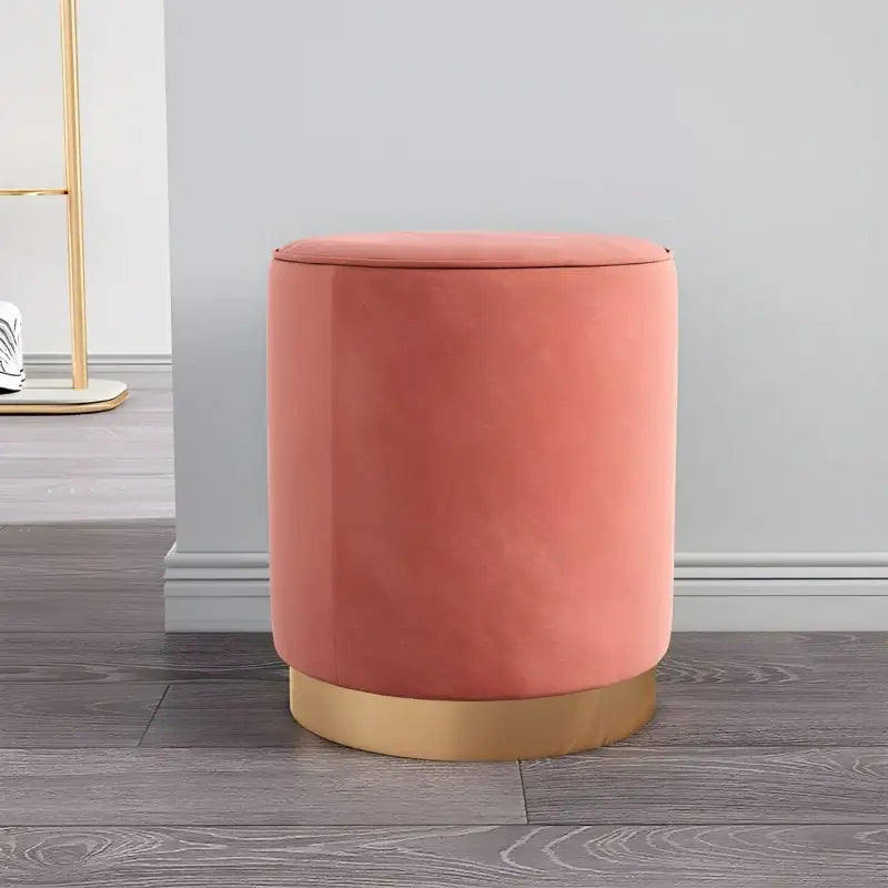 Coral-colored ottoman with gold base on a wooden floor