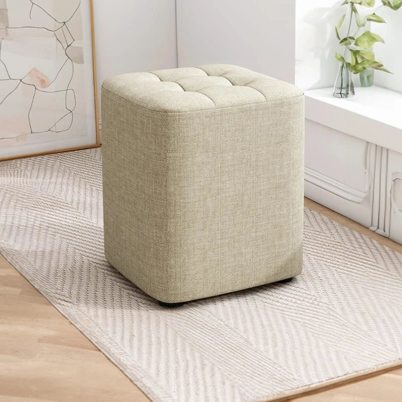 Beige cube ottoman on a patterned rug in a room setting.