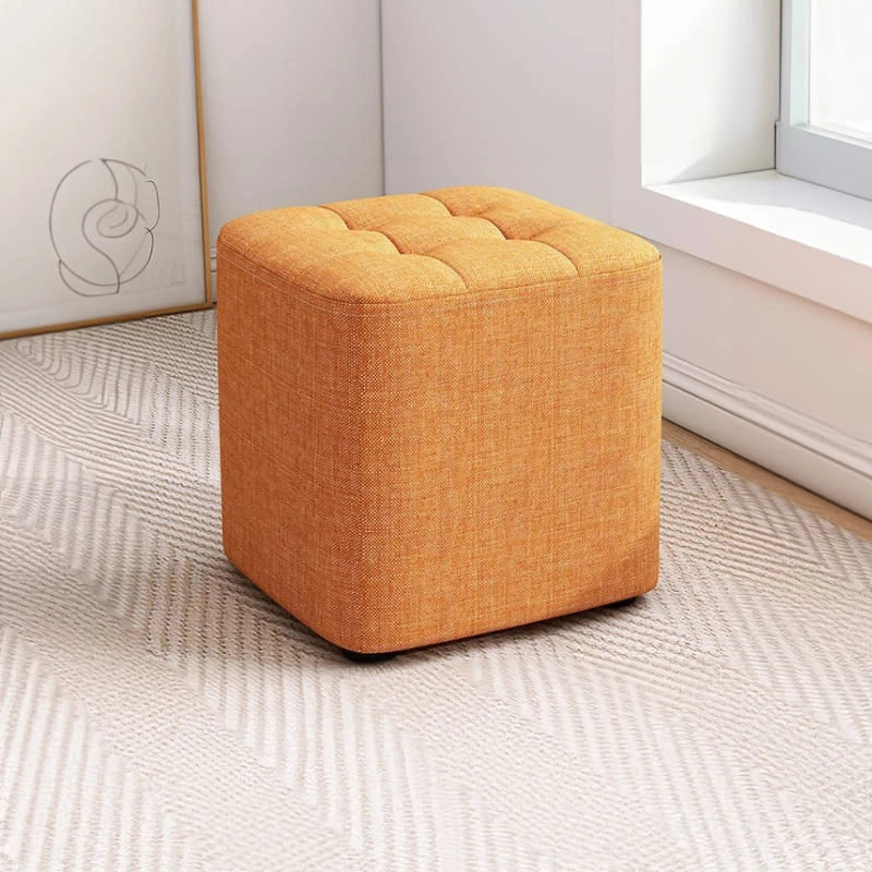 Orange ottoman on a textured floor with a light-colored wall in the background