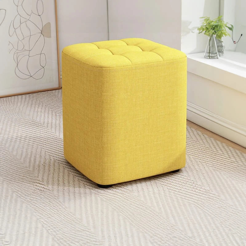 Yellow ottoman on a textured floor with a neutral wall and plant in the background
